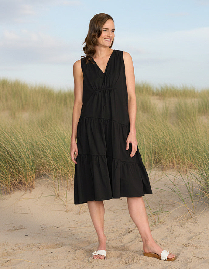 Woman in a black dress standing on a sandy beach with grasses in the background