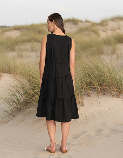 Woman in a black dress standing on a sandy dune with grasses.