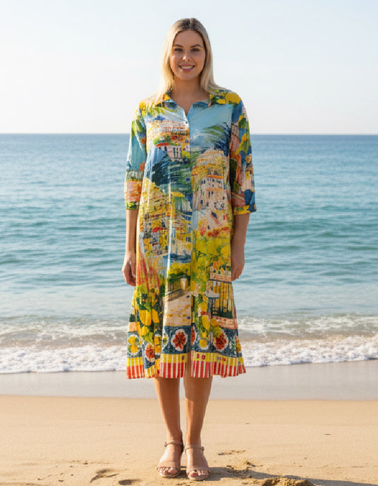 Woman wearing a colorful dress with a scenic print on a beach.