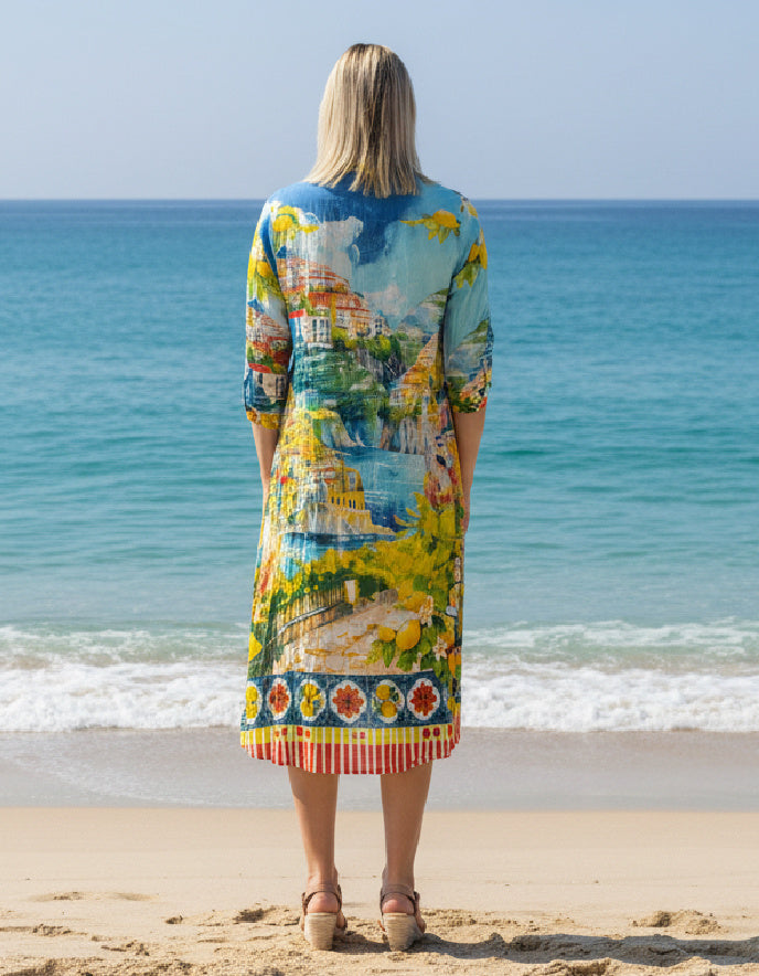 Woman wearing a colourful dress with a scenic print, standing on a beach.