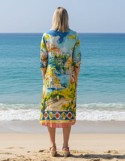 Woman wearing a colourful dress with a scenic print, standing on a beach.
