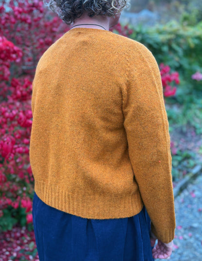 Person wearing a mustard yellow sweater with a blurred background of pink flowers and greenery