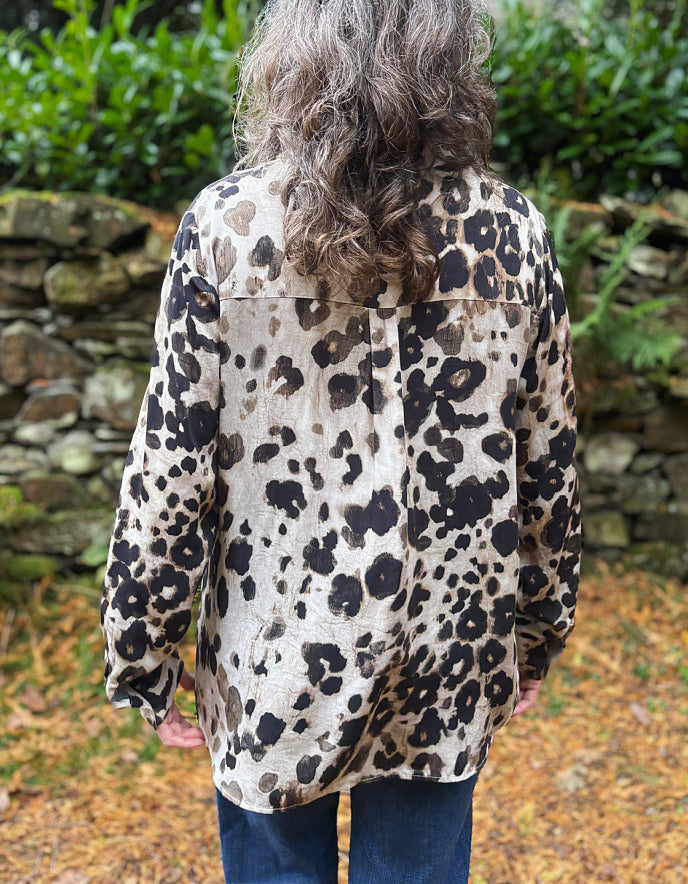 Person wearing a leopard print jacket standing in front of a stone wall and greenery
