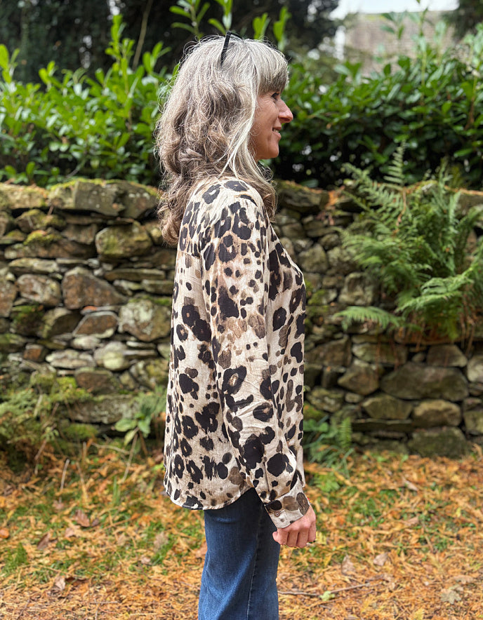 Person wearing a leopard print jacket standing in a garden with a stone wall and greenery.