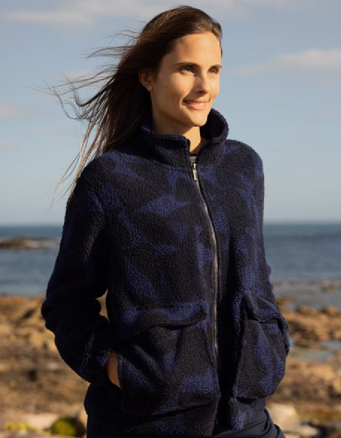 Woman wearing a dark blue jacket standing on a rocky beach with ocean and sky in the background