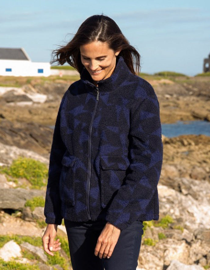 Woman wearing a blue patterned jacket standing on a rocky coastal landscape.