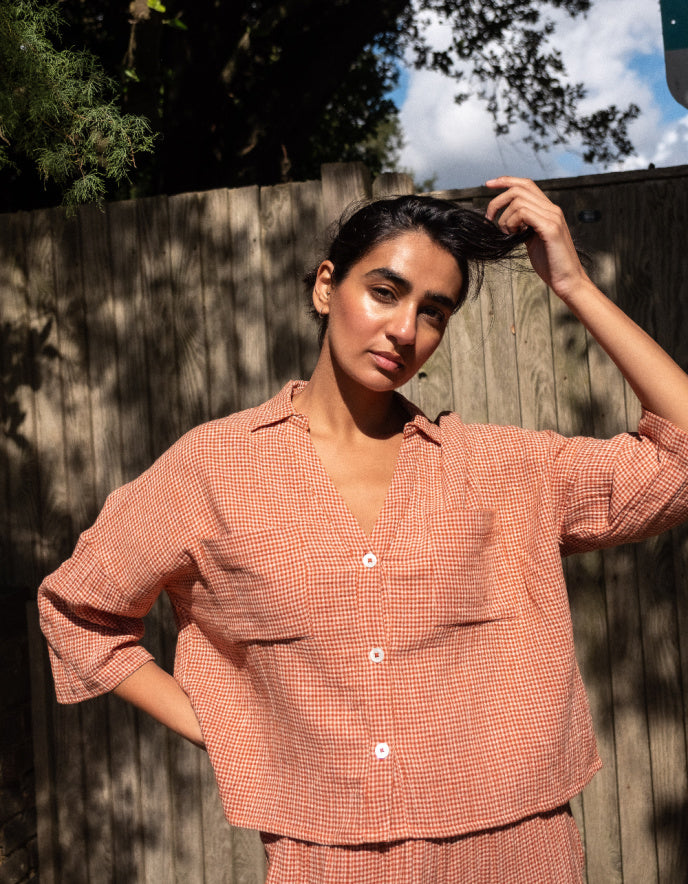 Woman wearing a peach-colored checkered outfit standing outdoors with trees in the background