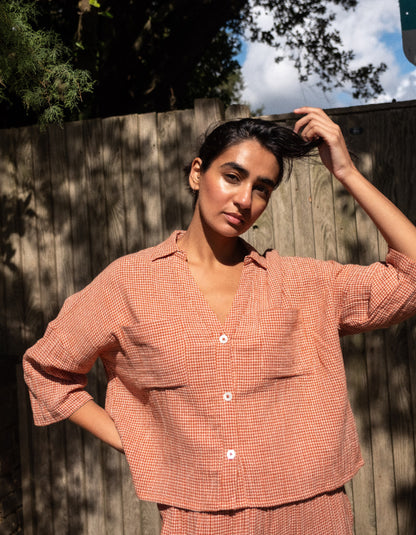 Woman wearing a peach-colored checkered outfit standing outdoors with trees in the background