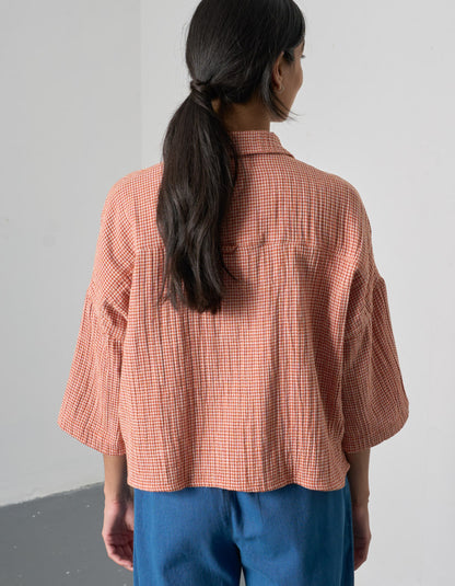 Person wearing a pink checkered shirt and blue pants against a gray background