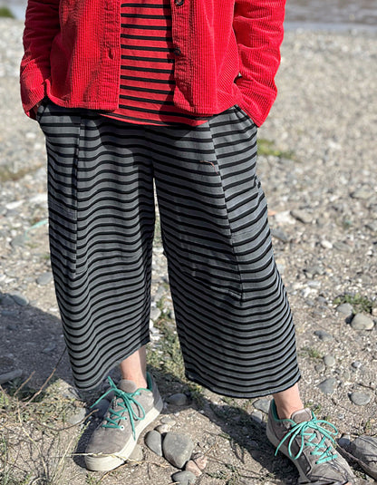 Person wearing a red jacket, striped shirt, and wide-leg pants standing on a rocky ground.