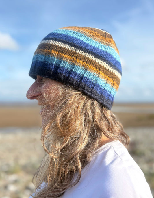 Person wearing a striped knit beanie on a beach with a clear sky.