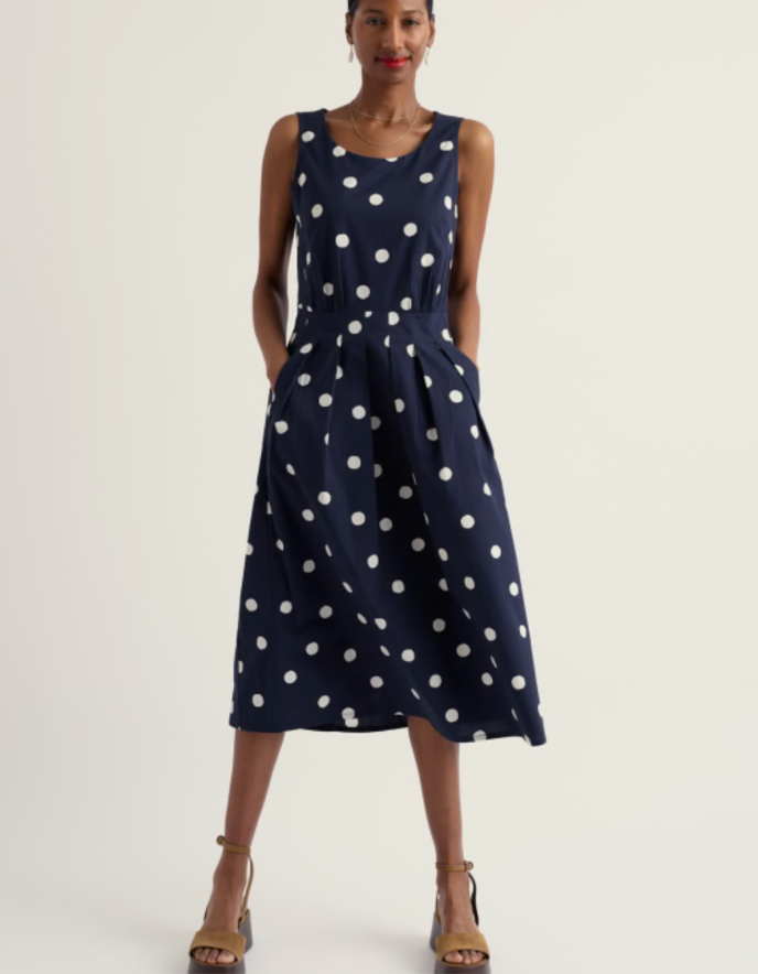 Woman wearing a navy dress with white polka dots on a plain background