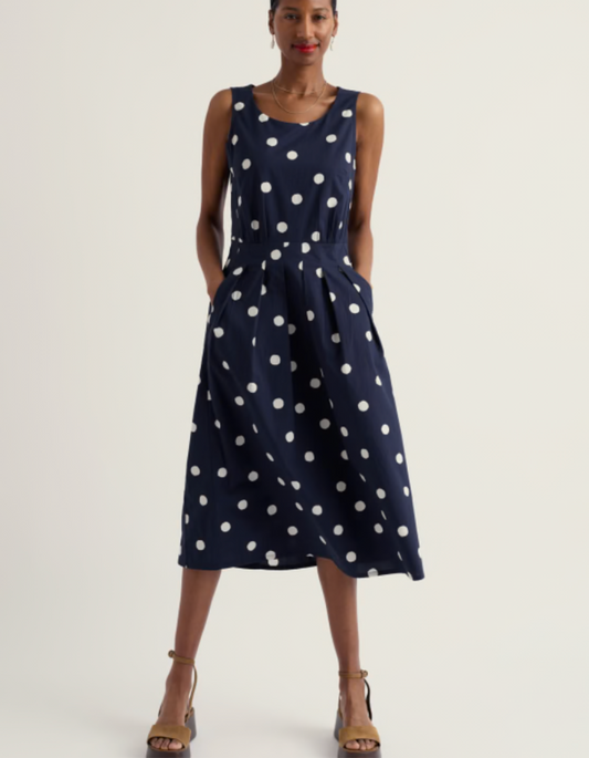 Woman wearing a navy dress with white polka dots on a plain background