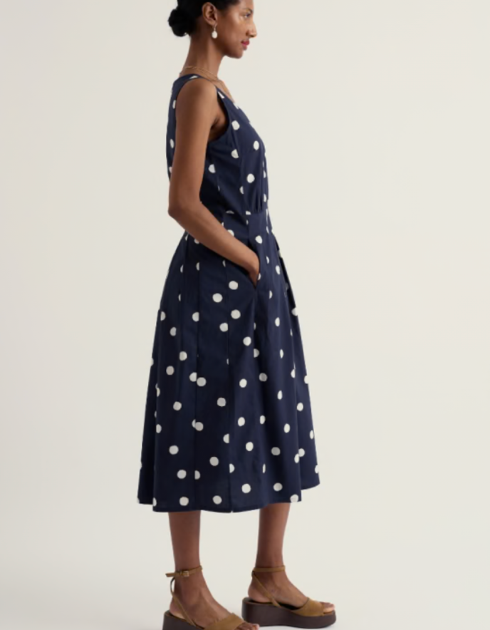 Woman wearing a navy dress with white polka dots on a plain background