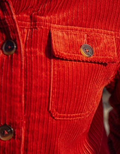 Close-up of a red corduroy jacket with buttons and a pocket.