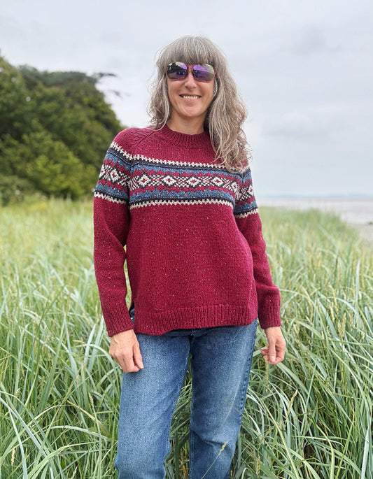 Person wearing a red Fair Isle patterned sweater standing in a grassy field
