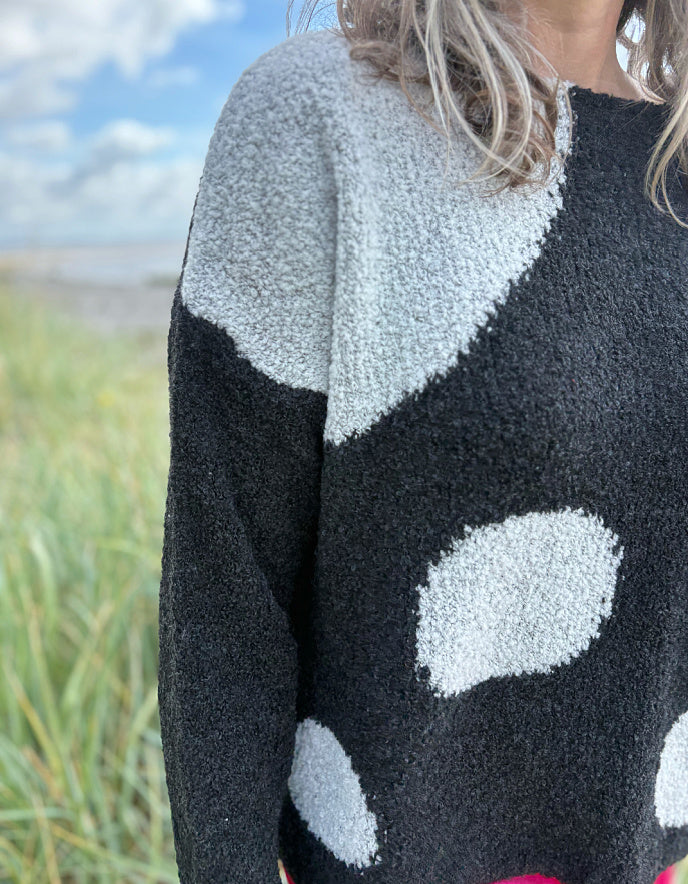 Woman wearing a black sweater with white polka dots and pink velvet pants standing on a beach.