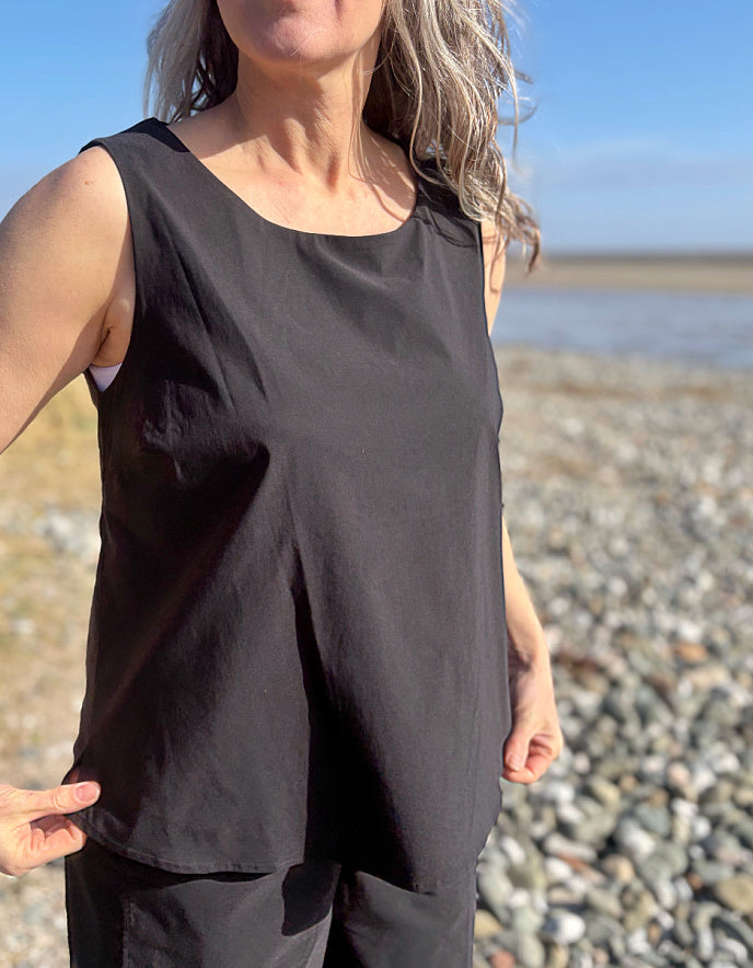 Person wearing a black sleeveless top and pants on a pebbly beach.