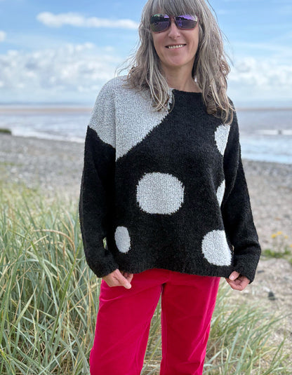 Woman wearing a black sweater with white polka dots and pink velvet pants standing on a beach.