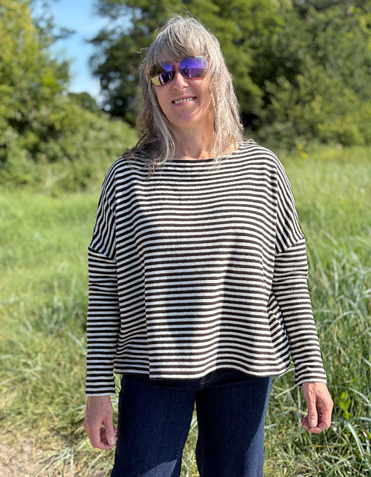 Woman wearing a black and white striped shirt and sunglasses in a grassy field.