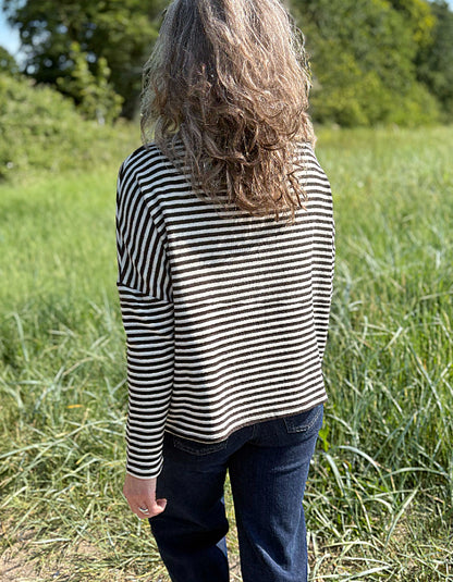 Woman wearing a black and white striped shirt and sunglasses in a grassy field.