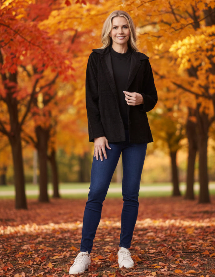Woman in black coat and blue jeans standing in an autumn park with colorful trees.