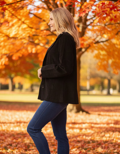 Woman in a black coat standing in an autumn park with colorful trees.