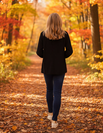 Person walking away on a leaf-covered path in a forest with autumn foliage.