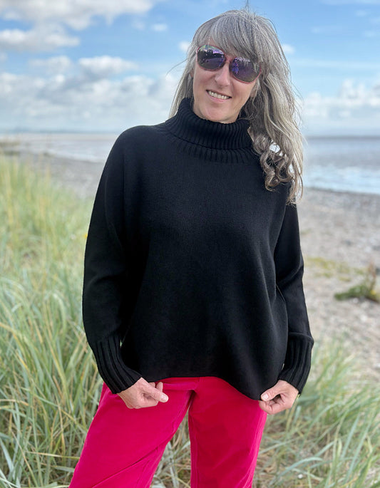 Person wearing a black turtle neck sweater and pink velvet pants standing on a beach.