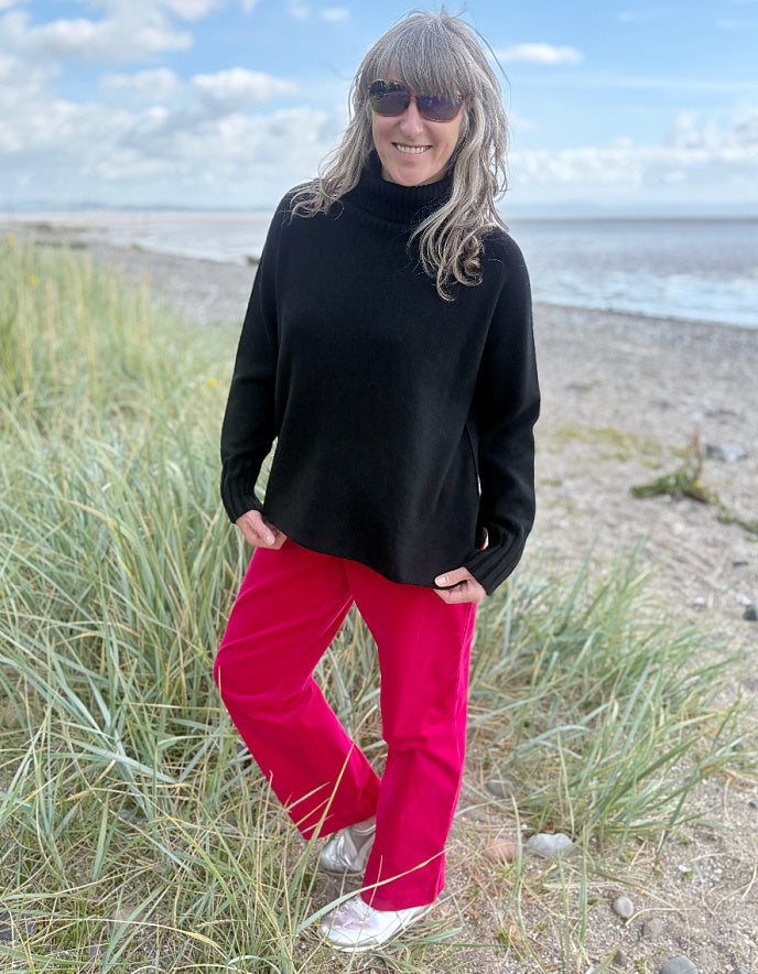 Person wearing a black turtle neck sweater and pink velvet pants standing on a beach.