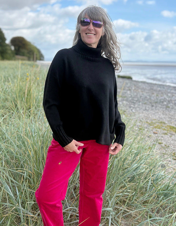 Person wearing a black turtle neck sweater and pink velvet pants standing on a beach.