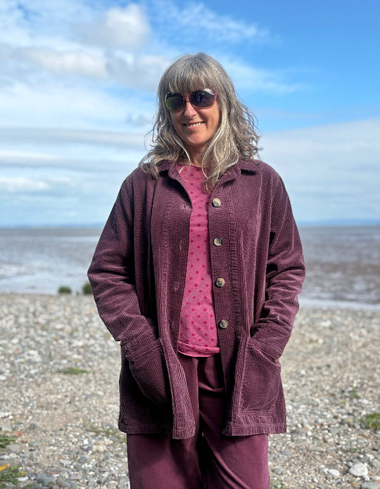 Woman standing on a beach wearing a purple jumbo corduroy blazer and pink shirt.
