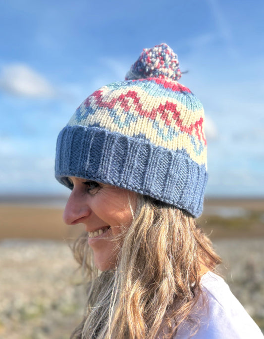 Person wearing a colorful knitted hat with a pattern against a blue sky.
