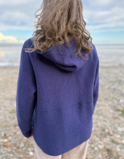 Person wearing a blue hooded boiled wool jacket on a beach