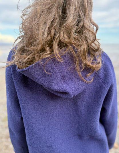 Person wearing a blue hooded boiled wool jacket on a beach