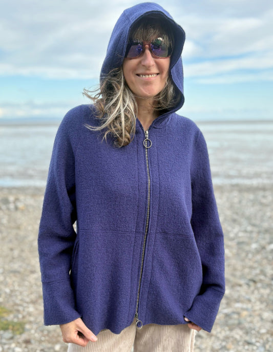 Person wearing a blue hooded boiled wool jacket on a beach