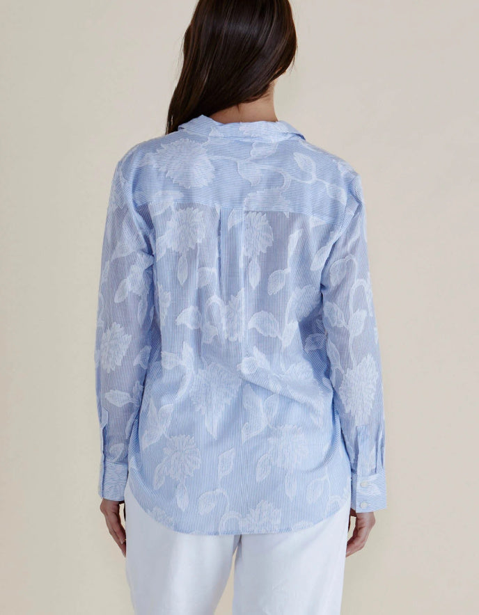 Woman wearing a light blue floral patterned shirt against a beige background