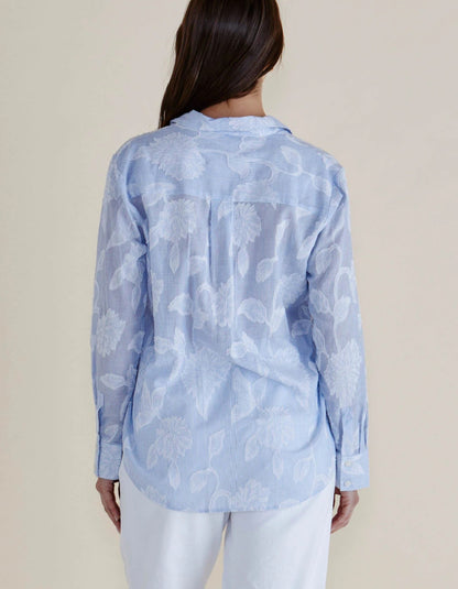 Woman wearing a light blue floral patterned shirt against a beige background