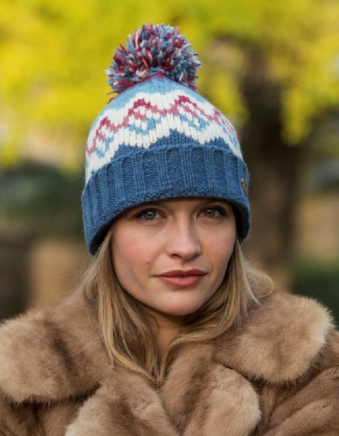 Woman wearing a blue knitted hat with a colorful pom-pom outdoors.