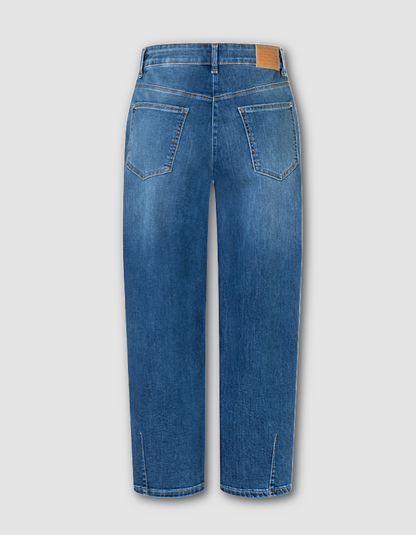 Blue denim jeans shown from the back, featuring a barrel-leg fit, classic five-pocket design, and a small tan leather patch on the back waistband, set against a solid light grey background.