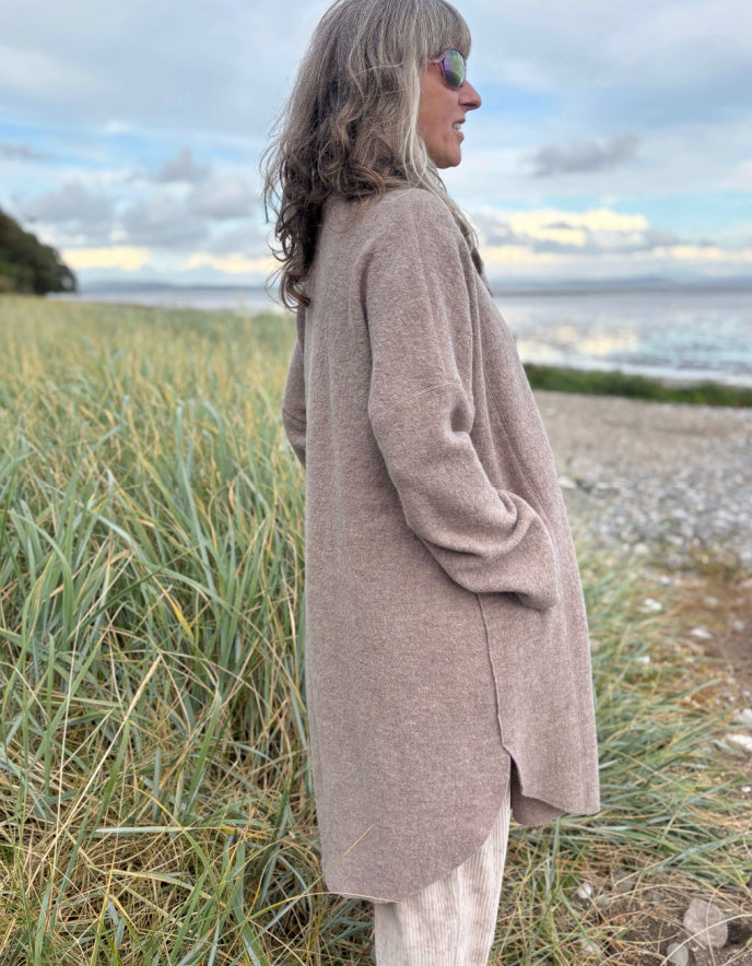 Woman wearing a beige boiled wool coat and sunglasses standing on a grassy beach.