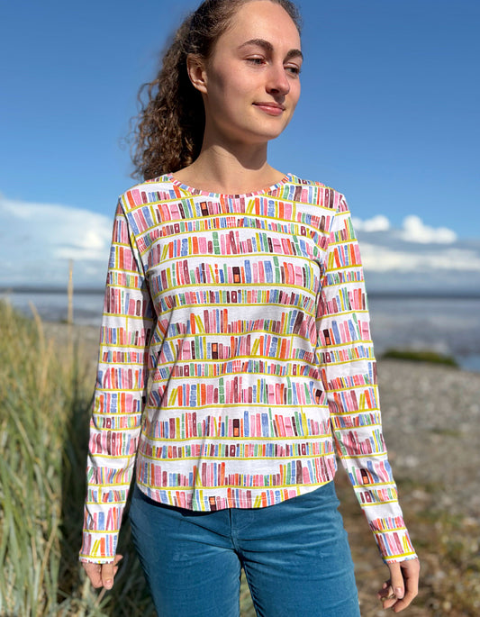 Woman wearing a colorful long-sleeve shirt with book pattern by a beach.