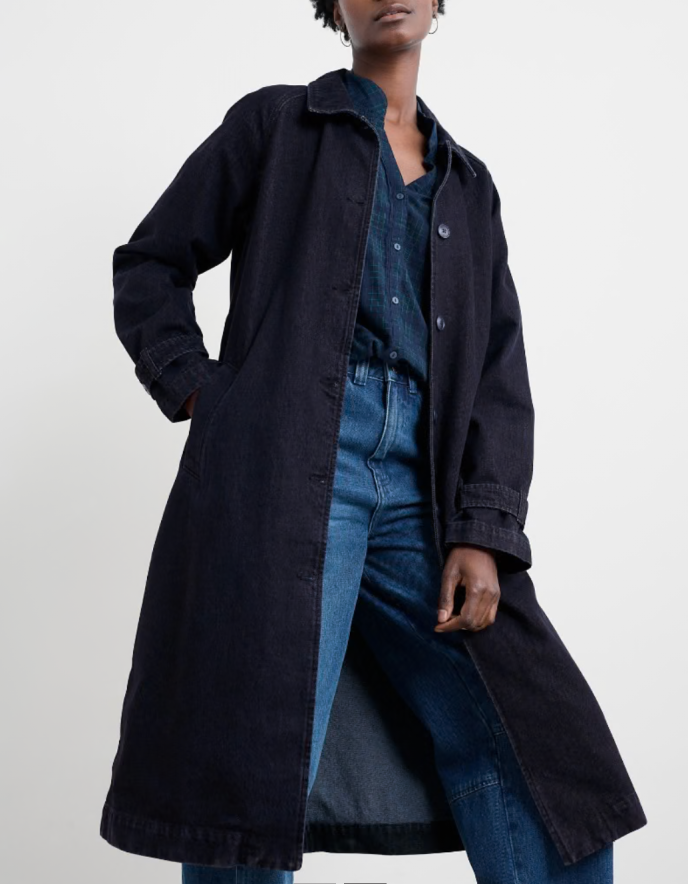 Person wearing a long dark coat over a denim outfit on a white background