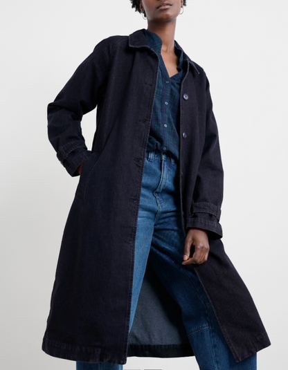 Person wearing a long dark coat over a denim outfit on a white background