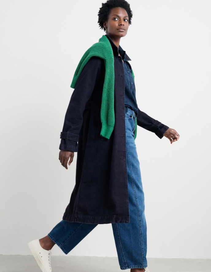 Person wearing a long dark coat, green scarf, and blue jeans on a white background