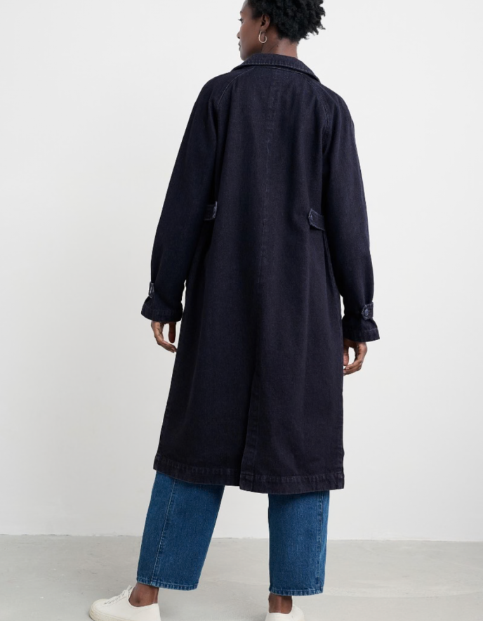 Person wearing a long dark coat and blue jeans on a white background