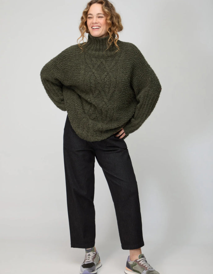 Person wearing a green sweater and black pants on a white background