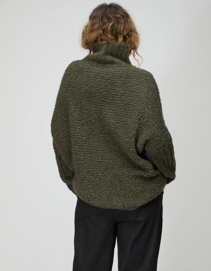 Person wearing a green knitted sweater and black pants on a white background