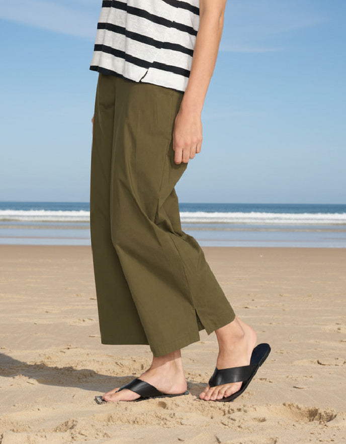 Person wearing green pants and black sandals on a beach