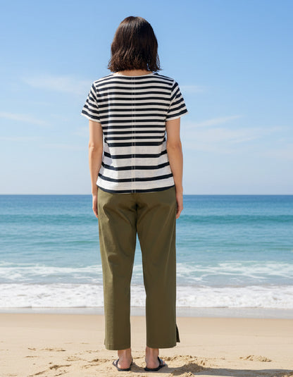 Person wearing a striped shirt and green pants standing on a beach with ocean view